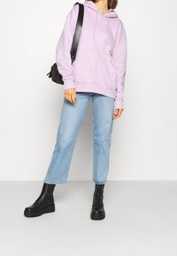 Felpa viola chiaro con tasca frontale, abbinata a jeans dritti blu chiaro e stivaletti neri con piattaforma e lacci. Borsa a tracolla nera.