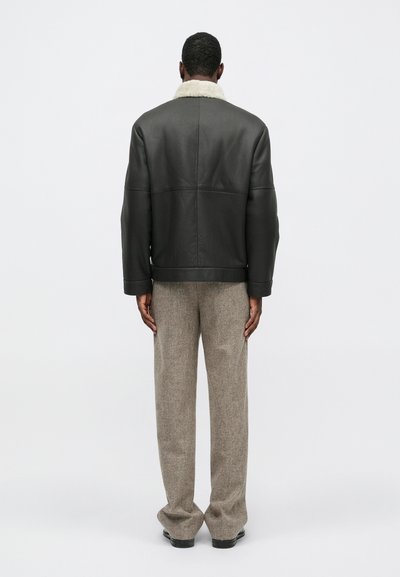 Tmavá kožená bunda s krémovým ovčím golierom, skombinovaná so šedými štruktúrovanými nohavicami. Strih je voľný s rovnou siluetou.