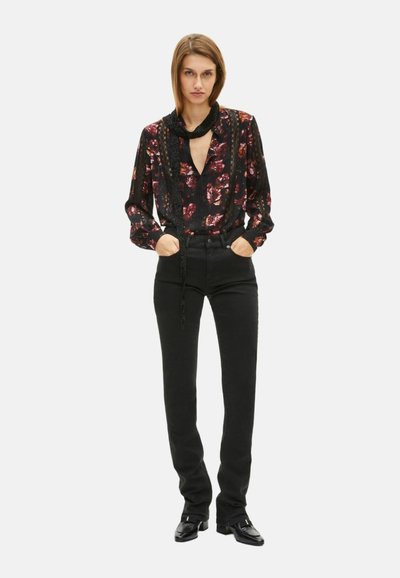 Blusa negra con flores y escote en V profundo, mangas fruncidas y detalle de lazo. Combinada con jeans negros ajustados y zapatos negros.