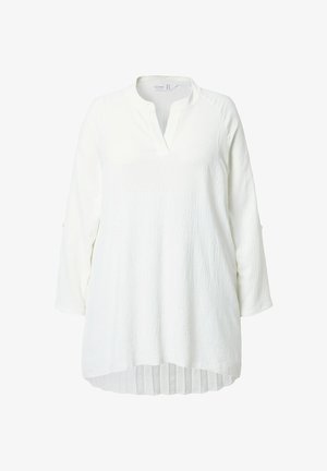 Bílá tunika s volným střihem, texturovanou látkou a výstřihem do V. Má dlouhé rukávy a řasený okraj pro zdůraznění detailů.