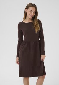Pletené hnedé šaty s priliehavým korzetom a skladanou sukňou, s dlhými rukávmi a okrúhlym výstrihom. Mäkka textura, elegantný dizajn.