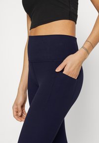 Mørkeblå høytliv leggings laget av et elastisk stoff, med en sidelomme og flate sømmer for komfort og bevegelighet.