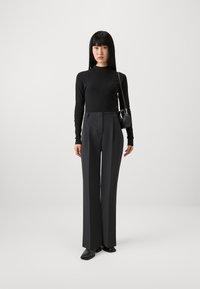 Sort ribbet langærmet top parret med højhalsede, brede grå bukser. Accessories inkluderer en lille sort håndtaske og spidse loafers.