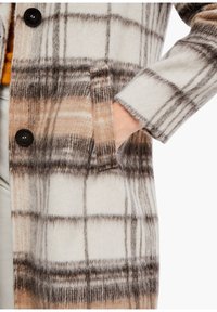 Abrigo de mezcla de lana con un gran patrón de cuadros en crema, marrón y gris, con cierre de botones y un bolsillo lateral. Textura suave.
