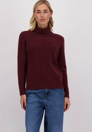 Pull bourgogne avec un col montant, motif en losanges texturé, poignets et ourlet côtelés. Associé à un jean ample bleu clair.