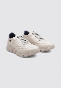 Zapatillas de cuero blancas con un diseño acolchado, suela de goma, cordones grises y un forro interior azul. Presenta un logo en el lateral.