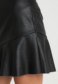 Schwarzer Kunstlederrock mit ausgeflocktem Saum, glatter Textur und subtiler Satinoptik sowie Nahtdetails entlang der Taille.