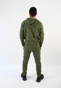 Sudadera de color verde oliva con capucha ajustable, combinada con joggers a juego que tienen franjas laterales. El material parece suave y tiene un corte relajado.
