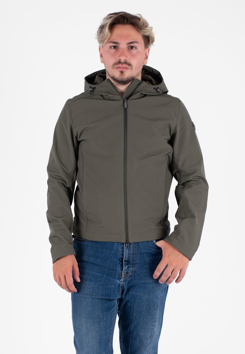 Giacca verde oliva con zip completa e cappuccio, caratterizzata da una texture liscia e toggles regolabili, abbinata a jeans blu.