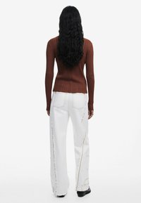 Rusten ribbet langærmet top sat sammen med højtaljede hvide denim jeans med flossede kanter og kontrastsyninger. Sorte hælede støvler.