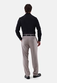 Schwarzes Langarmshirt und hellbeige Hose, beide in taillierter Passform. Die Hose hat Gesäßtaschen und ein dezentes Muster. Schwarze Schuhe vervollständigen das Outfit.