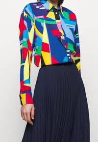 Kolorowa koszula z długim rękawem z geometrycznymi wzorami w niebieskim, czerwonym, żółtym i zielonym kolorze, z listwą guzikową i kołnierzykiem.