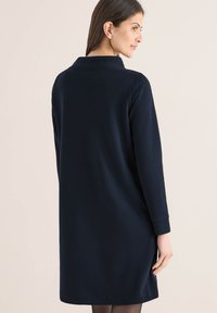 Robe bleu marine à manches longues avec col, tissu texturé et coupe décontractée, présentant un ourlet droit et des fentes latérales discrètes.