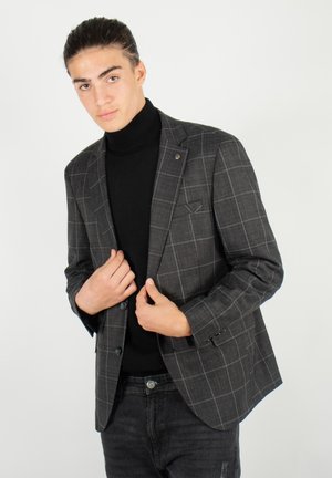 Blazer à carreaux gris avec un bouton unique, revers à cran et poche poitrine. Porté sur un turtleneck noir et associé à un jean foncé.