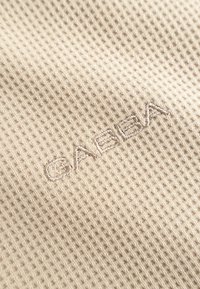 Nærbillede af beige stof med vaffelstruktur med ordet "CABIN" broderet med tråd i samme farve.