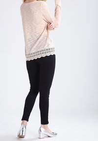 Ljusrosa långärmad topp med texturerad tyg och spetsdetalj, i kombination med svarta slim-fit-byxor och silvriga klackskor.