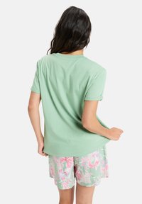 Lys grøn t-shirt med oprullede ærmer, parret med pastelfarvede blomstershorts, der har pink og grønne mønstre. Blød, afslappet design.