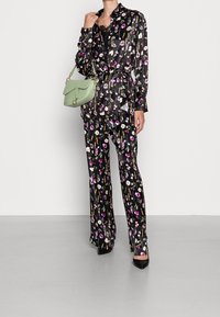 Black floral satin pantsuit with long sleeves, featuring a belt and lace inset. Paired with a light green handbag and black heels.