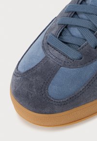 Gros plan d'une basket en daim bleu avec des lacets assortis et une semelle en caoutchouc marron clair texturée.