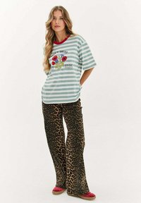 Pruhované mintově zelené a bílé tričko s červeným límcem, se květinovou grafikou. V kombinaci s leopardím potiskem, širokými kalhotami a červenými pantoflemi.