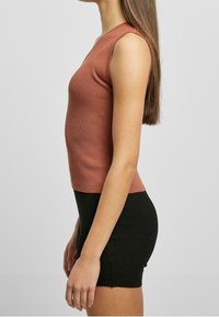 Rippstrick-Top in Rostfarbe, kombiniert mit einem schwarzen, gerippten Minirock. Der Stoff hat eine strukturierte Optik und eine enganliegende Passform.