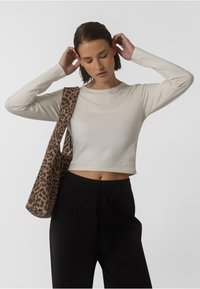 Kreemikadu pikkade varrukatega crop top, kombineeritud kõrge vöökohaga mustade pükstega ja leopardimustriga õlakotiga, millel on mugav lõige.