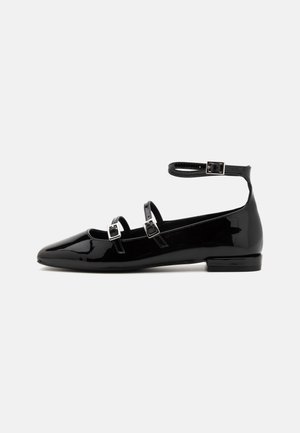 Schwarzer Lacklederschuh mit flacher Sohle und drei silbernen Schnallenriemen, darunter ein Fesselriemen, und niedrigem Absatz.