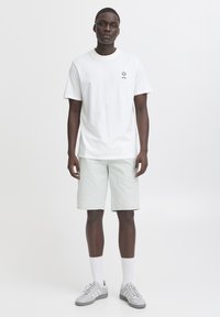 Bela bombažna majica s kratkimi rokavi z majhnim logotipom na prsih; svetlo zelene denim kratke hlače; sive superge; bele nogavice; priložnostna oblika in slog.