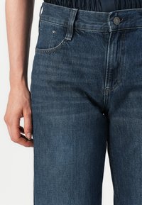 Donkerblauwe denim jeans met een klassiek vijf-pocket ontwerp. Voorzien van een knoop- en ritssluiting, met zichtbare stiksels en een gladde textuur.