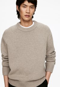 Heller beiger Strickpullover mit Rundhalsausschnitt, gerippten Bündchen und lässiger Passform. Hergestellt aus einem strukturierten Stoff.