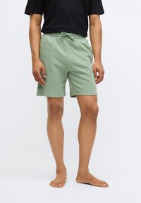 Pantaloni scurți de un verde deschis, dintr-un material texturat, dotati cu un elastic la talie și șnur, concepuți pentru confort și libertate de mișcare.