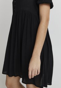 Svart klänning i lätt tyg, med korta puffärmar, en figurnära bodice med knappar och en fladdrande kjoldesign.