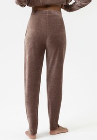 Bruine, zachte velvet broek met een ontspannen pasvorm, rechte pijpen en een tailleband. Bevat zijsplitsingen aan de zoom voor extra detail.