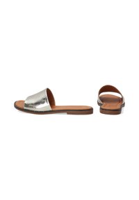 Metalické stříbrné sandály na ploché hnědé podrážce. Otevřená zadní část a široký design popruhu mají hladký povrch a minimální švy.