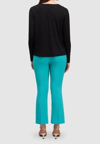 Haut noir à manches longues associé à un pantalon évasé turquoise et des sandales à talons beiges, vu de dos sur un fond gris.