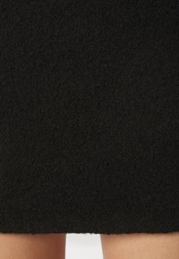 Gros plan d'une jupe texturée noire s'arrêtant au-dessus des genoux avec la peau des jambes visible en dessous.