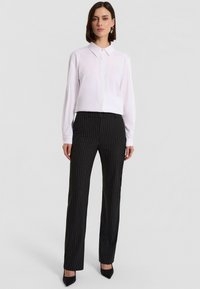 Biała koszula z długim rękawem z zapięciem na guziki w połączeniu z czarnymi spodniami w prążki. Czarne buty na wysokim obcasie dopełniają całość.