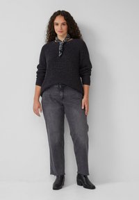 Dunkelgrauer Strickpullover mit rundem Halsausschnitt und gerippter Textur, kombiniert mit grauen geraden Jeans, schwarzen Knöchelstiefeln und einem gemusterten Schal.