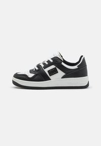 Sneaker low-top in bianco e nero con materiale in pelle, punta perforata, lacci bianchi piatti e suola in gomma nera. Presenta dettagli del logo sui lati.