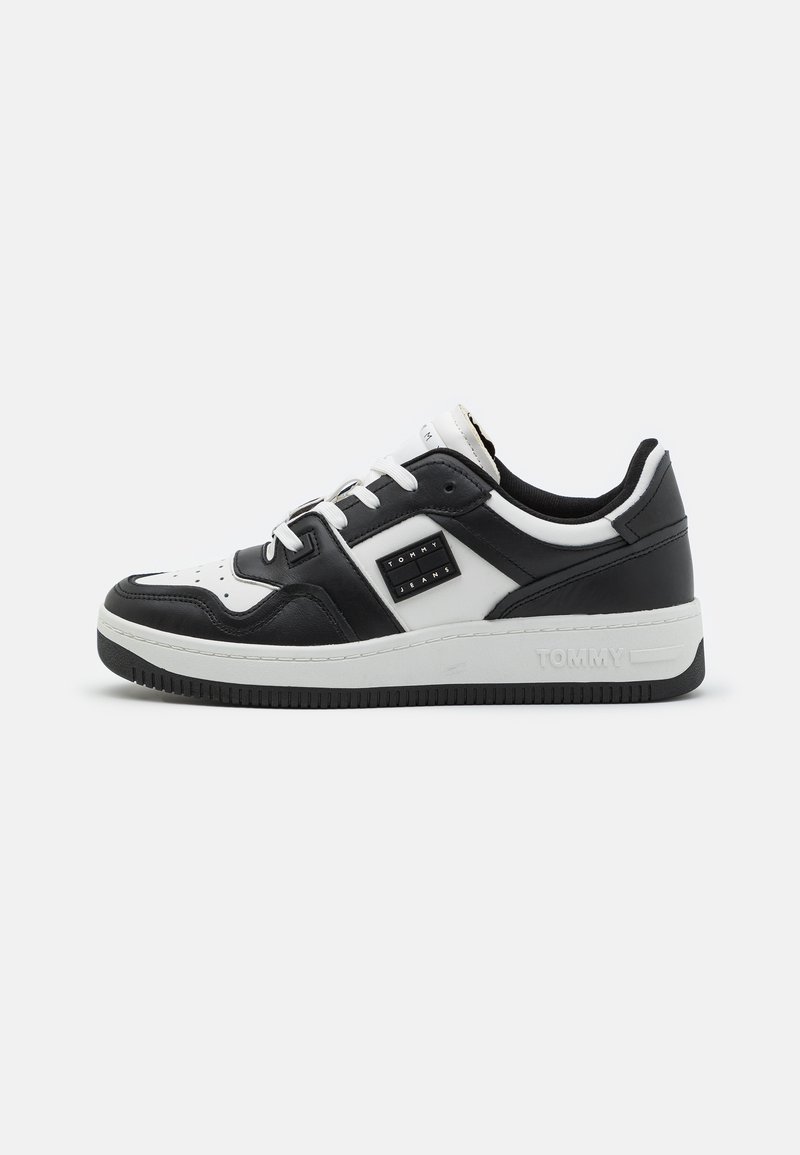 Sneaker low-top in bianco e nero con materiale in pelle, punta perforata, lacci bianchi piatti e suola in gomma nera. Presenta dettagli del logo sui lati.