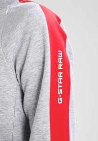 Gray sweatshirt with a red accent stripe along the sleeve, featuring white "G-STAR RAW" logo. Material appears soft and textured.
