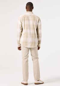Beige geruite shirt met knoopmanchetten, lichte stof en een relaxte pasvorm. Gecombineerd met crèmekleurige broek en witte sneakers.