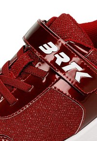 Czerwone buty sportowe z teksturowaną siateczką górną i błyszczącymi akcentami z lakierowanej skóry. Posiadają system sznurowania oraz rzep z białym logo.