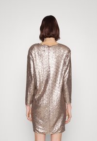 Robe à manches longues, arrivant au genou, en sequins dorés roses avec un col rond et une texture de tissu lisse. Une couture part en ligne droite le long du dos.