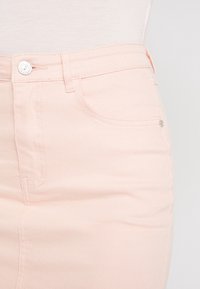 Svetle růžová džínsová sukně s přiléhavým designem, předními kapsami a stříbrnými knoflíky. Hladká textura s viditelnými švy.