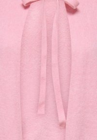 Pull rose pâle avec un tissu doux et texturé, fermeture nouée au niveau du col et design ouvert à l'avant.