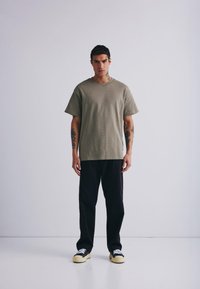 Olivenfarget bomull T-skjorte med korte ermer, kombinert med svarte bukser. Svarte og hvite sneakers fullfører det avslappede antrekket.