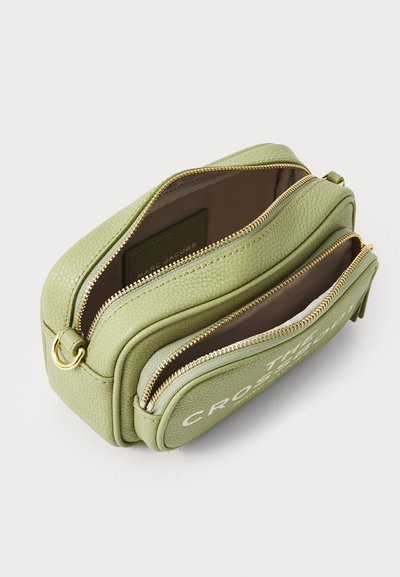 Zelená kožená crossbody taška s texturou a dvěma zipovými přihrádkami, doplněná zlatým kováním. Na přední straně je vyražené logo.
