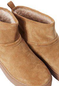 Bottines à cheville en daim beige avec une doublure intérieure douce, un bout arrondi et une semelle en caoutchouc plate, comprenant des accents cousus et une languette de maintien.