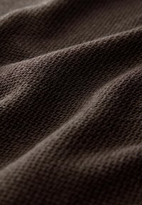 Un tissu marron texturé avec un motif en nid d'abeille ; un matériau doux et tricoté aux nuances variées et aux plis ondulés, mettant en valeur ses qualités tactiles.